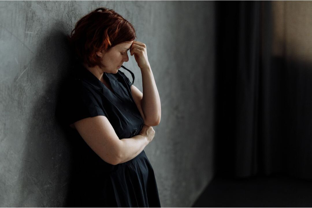 stressed woman leaning against a wall taking a deep breath to regulate her nervous system