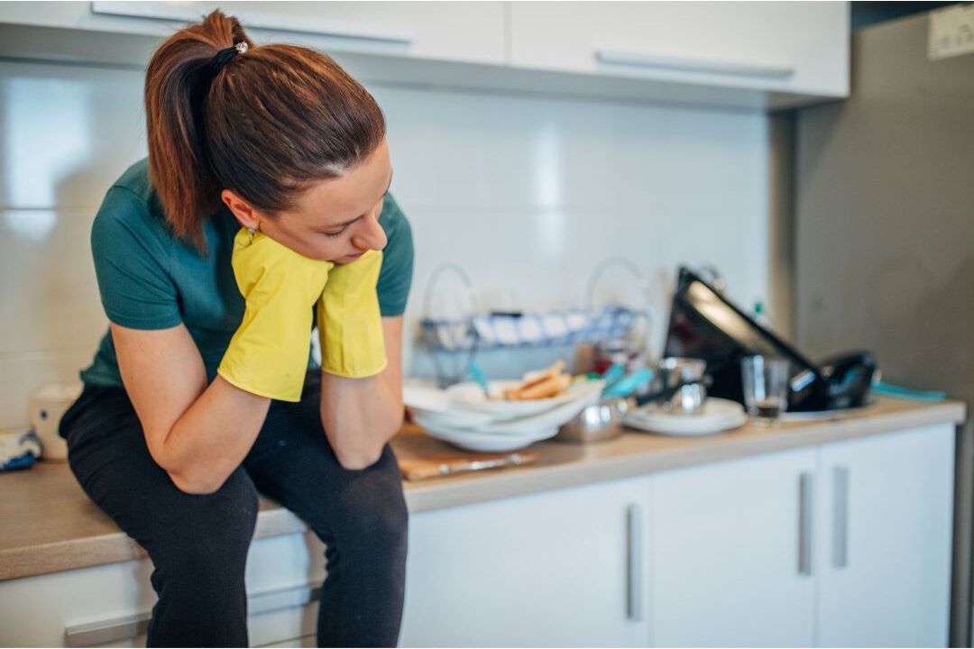 overwhelmed woman looking at a cluttered kitchen counter showing household chaos triggers