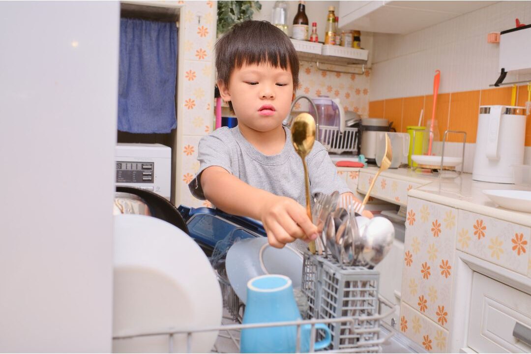 child putting a dish in the dishwasher illustrating simple household rules that keep your kitchen clean