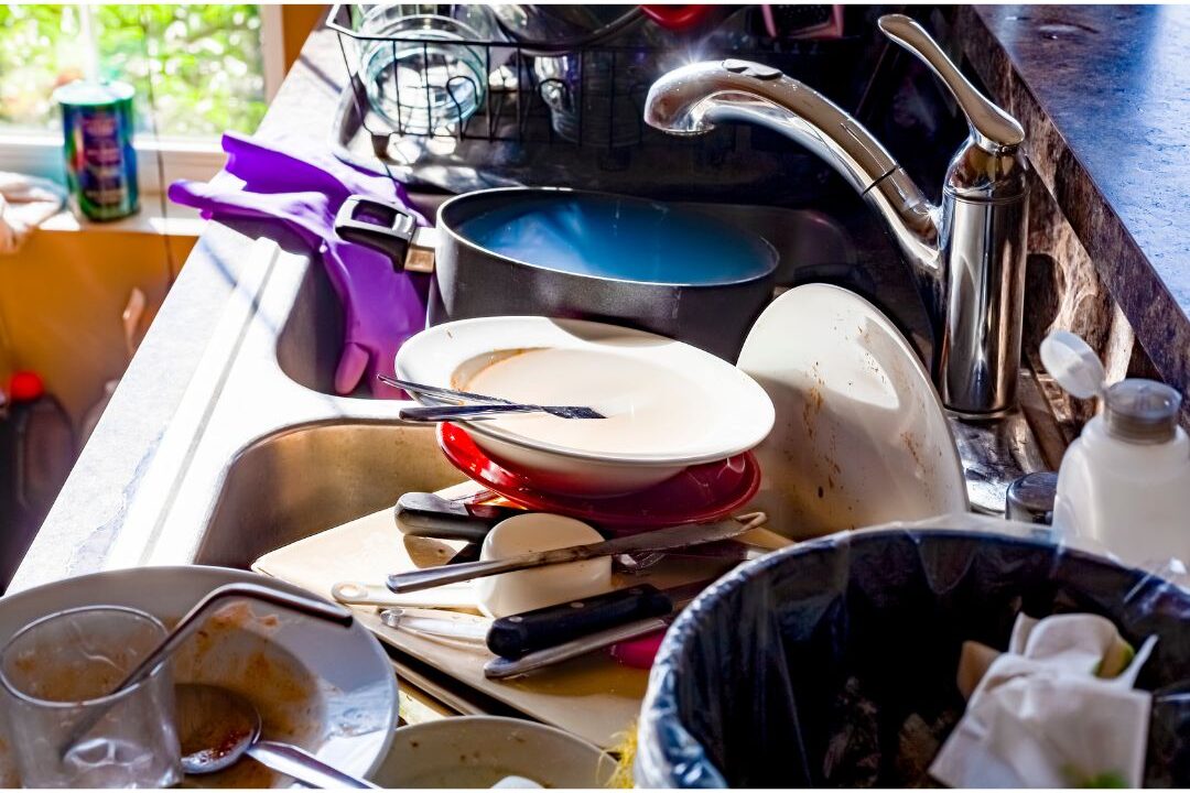 dirty dishes piled high in kitchen sink showing a major reason your kitchen never stays clean