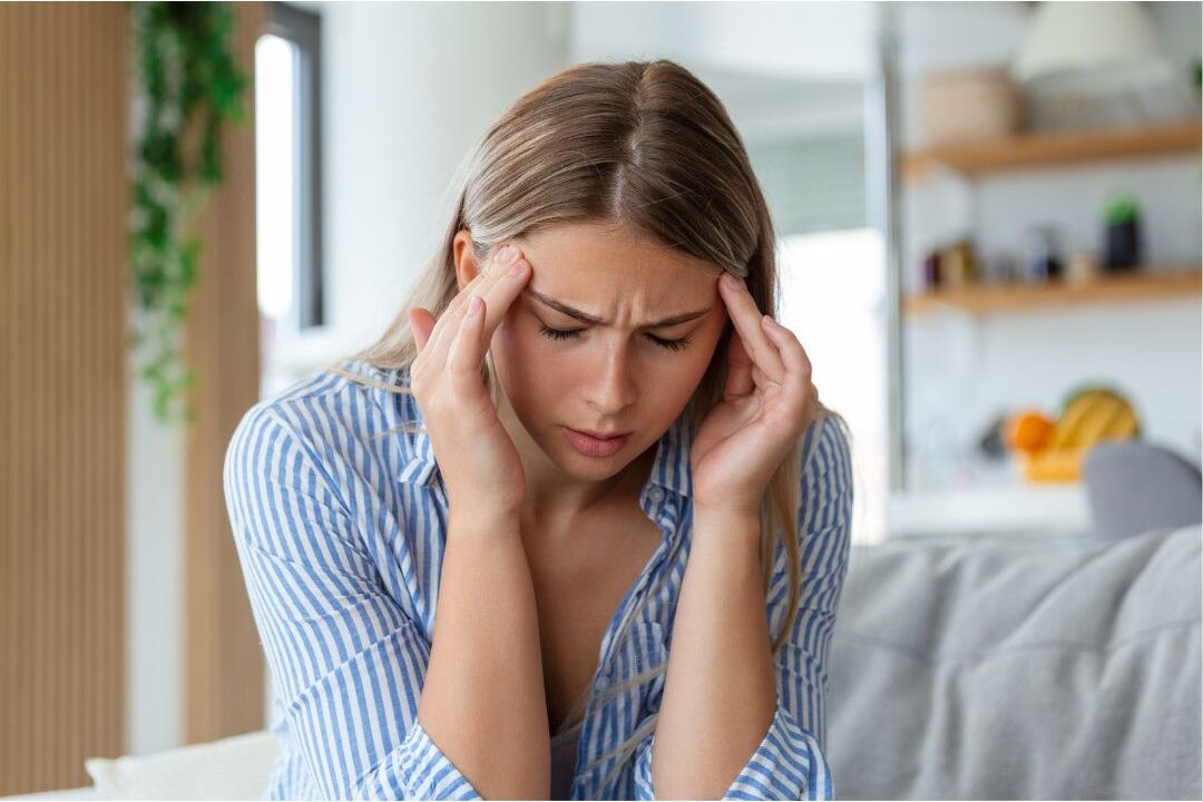 woman holding her head in pain illustrating physical symptoms of warning signs you're headed for mom burnout