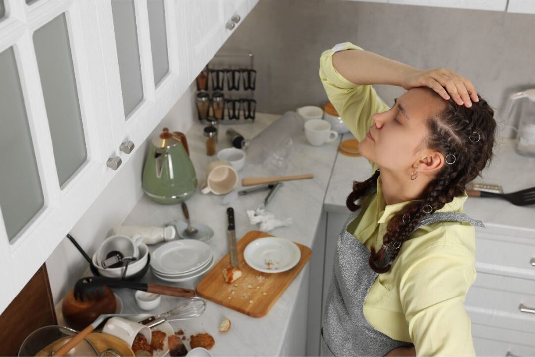 frustrated woman standing in a messy kitchen trying to figure out the real reason your kitchen never stays clean