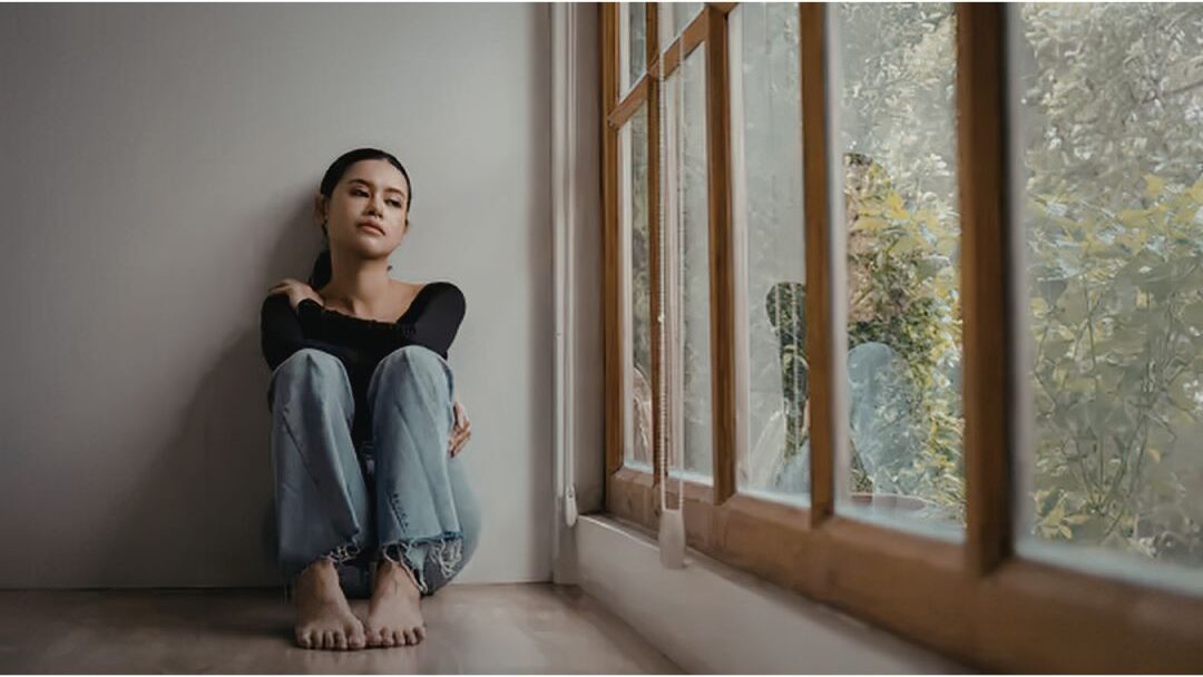 thoughtful woman sitting alone by a window dealing with internal rest guilt showing self-care mistakes that leave you exhausted