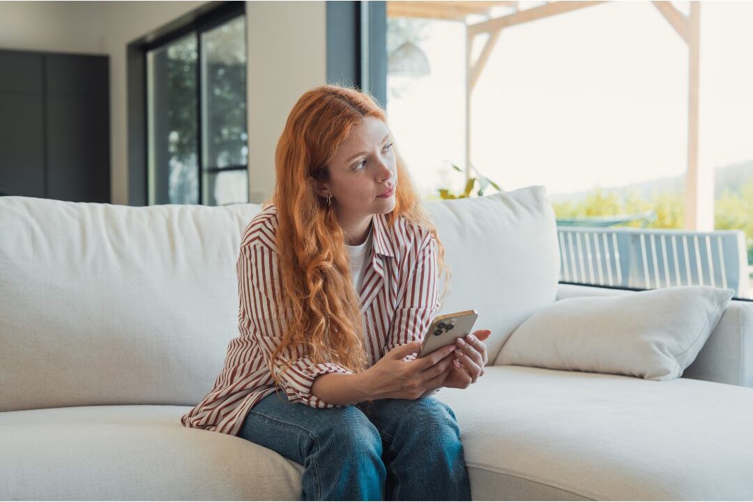 woman holding her phone contemplating a text response while isolating herself