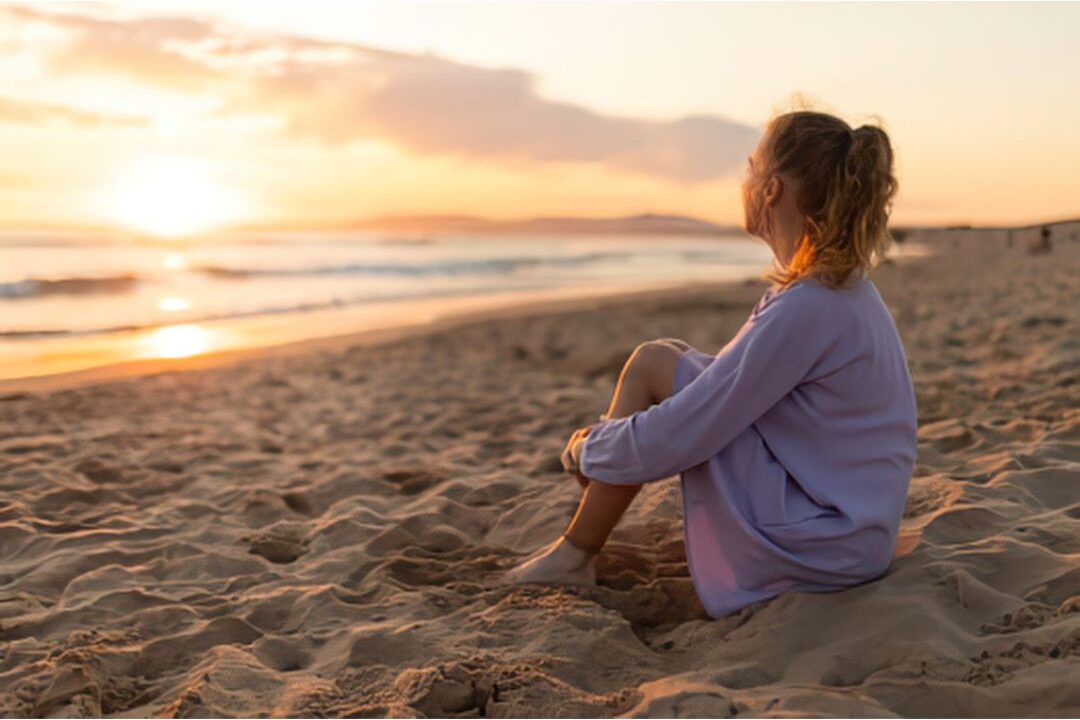 woman sitting on a beach watching the sunrise showing spiritual rest and connection