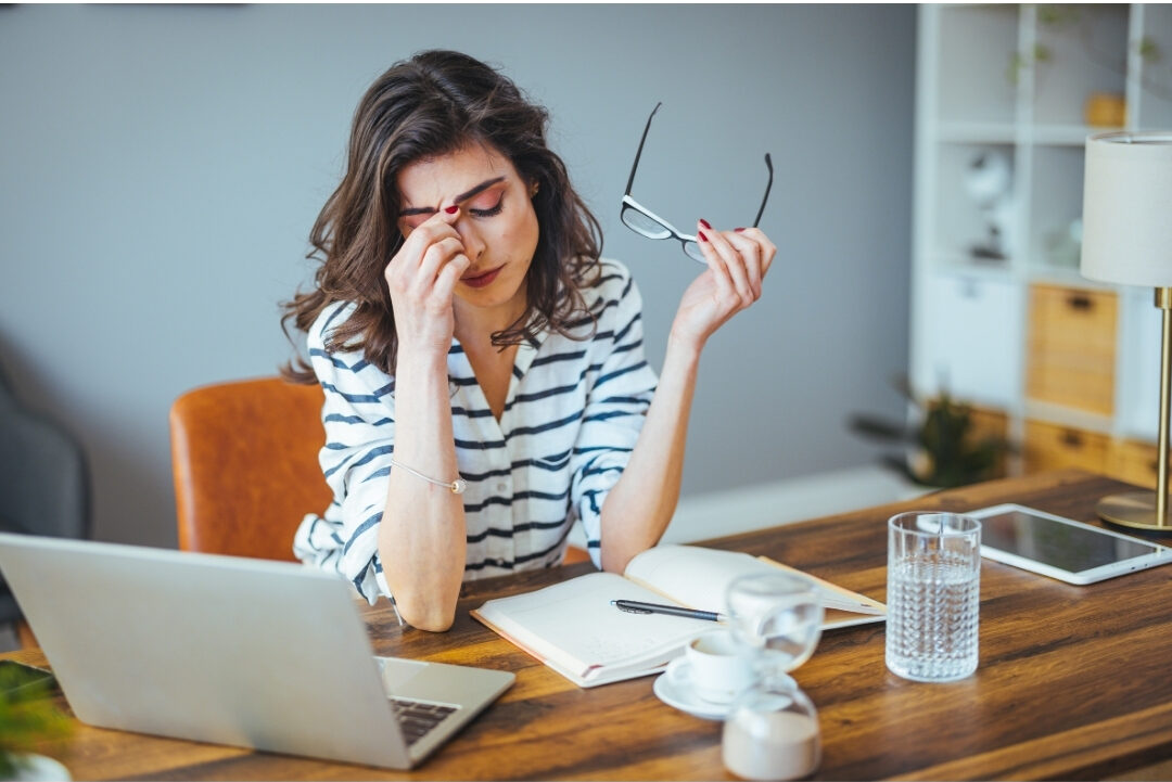 stressed woman sitting at laptop at messy dining table recognizing 10 mistakes that are killing your productivity at home