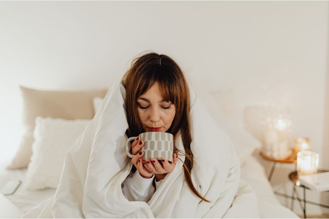 sick woman wrapped in a blanket drinking warm tea to boost immune recovery