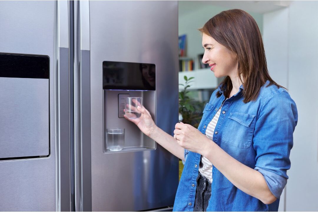 clean glass of water next to modern refrigerator dispenser showing automated filter replacement