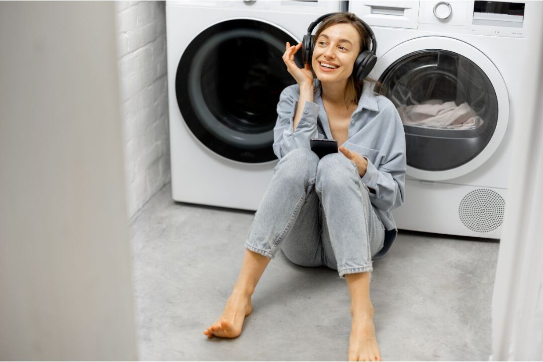 woman wearing headphones smiling while folding white linen laundry showing joyful chores