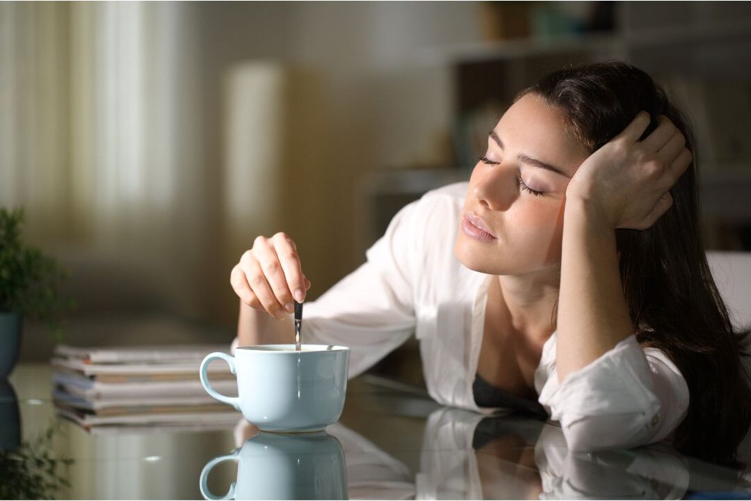 tired woman holding a coffee cup looking exhausted in her kitchen