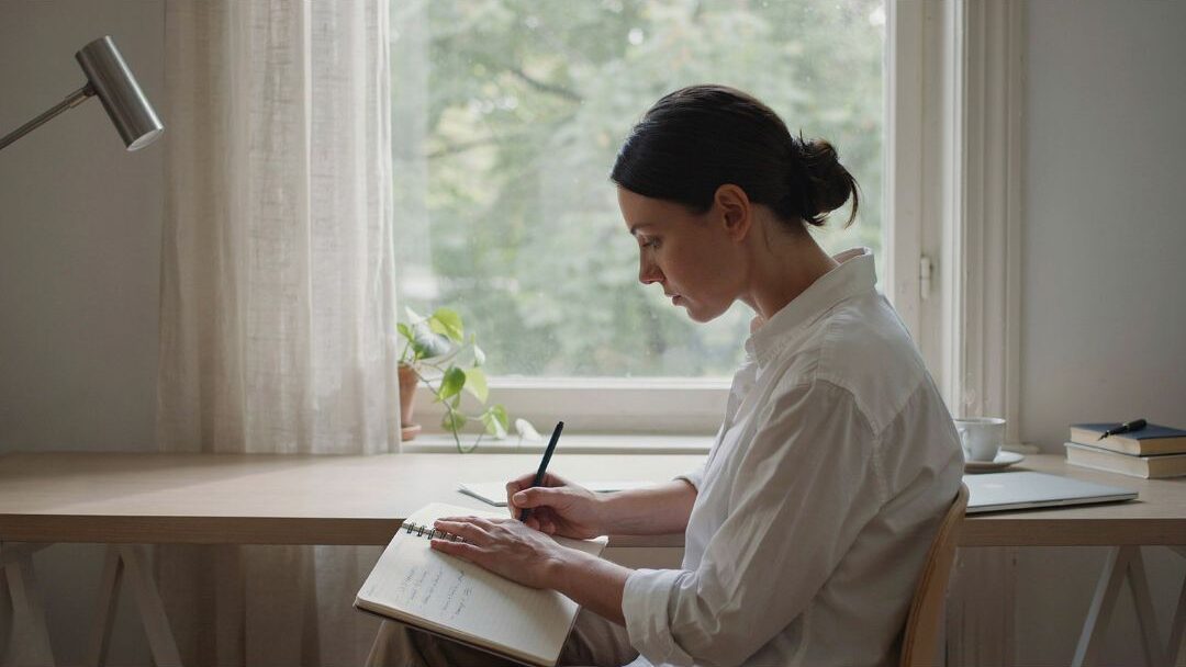 woman writing in a notebook at a clean white desk space executing a clear blogging strategy