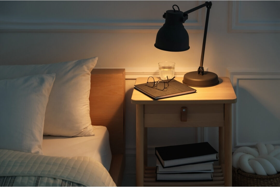 cozy bedroom with soft warm lamp light and book resting on nightstand showing digital free space learning how to work from home without feeling like you're working all day