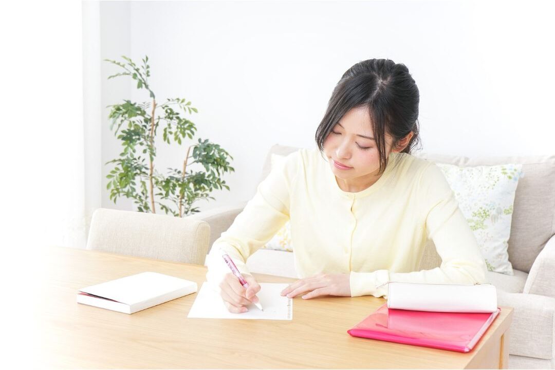 woman writing thoughtfully in a spiral notebook near a window
