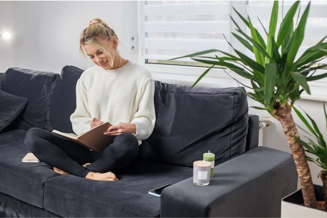 woman journaling quietly in a sunlit cozy living room corner practicing self-compassion