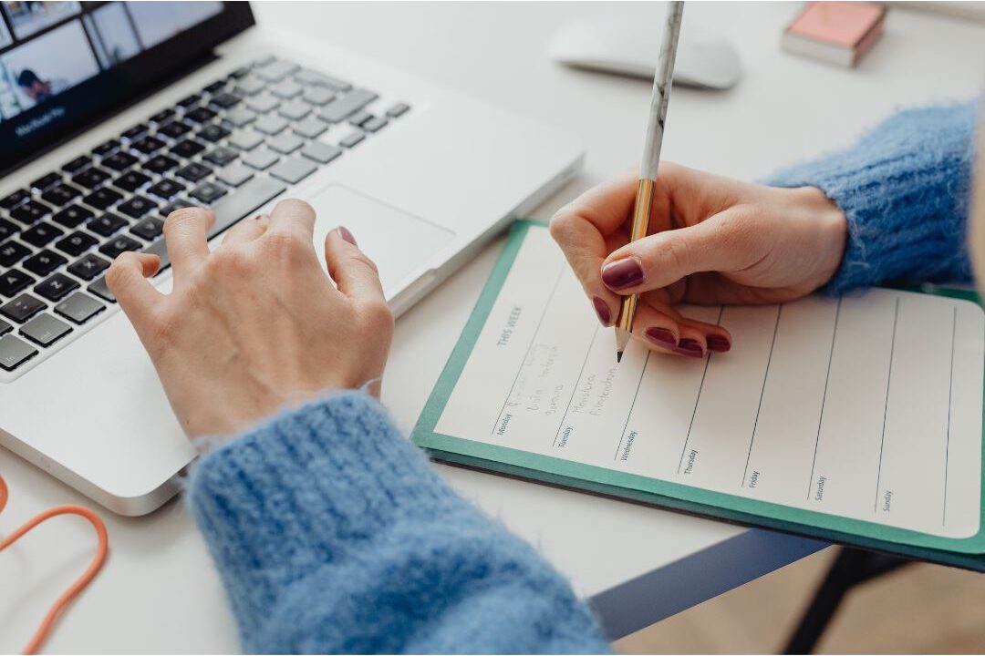 woman making a daily schedule in a paper planner at her desk