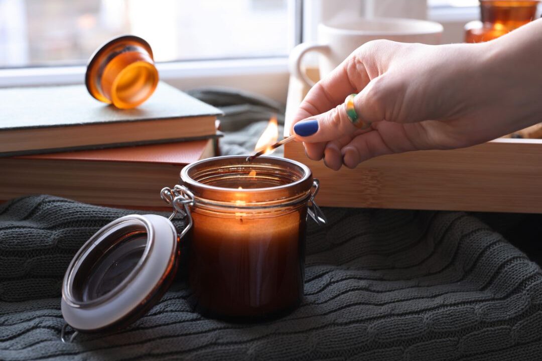 woman lighting a candle on a wooden side table near a sunlit window creating cozy mood
