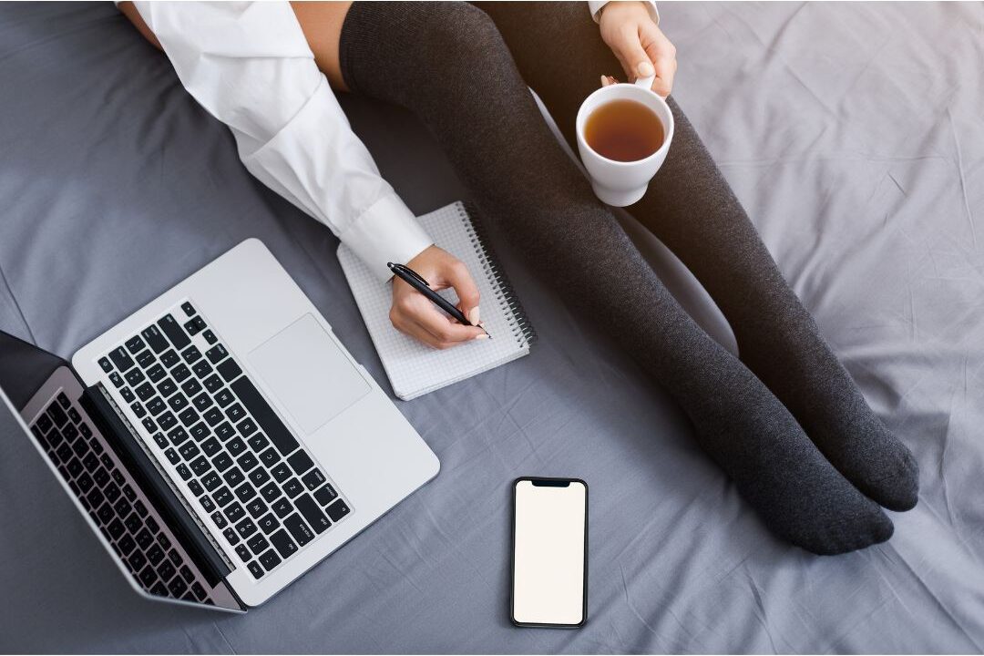 woman reviewing laptop notes with a cup of tea on her bed