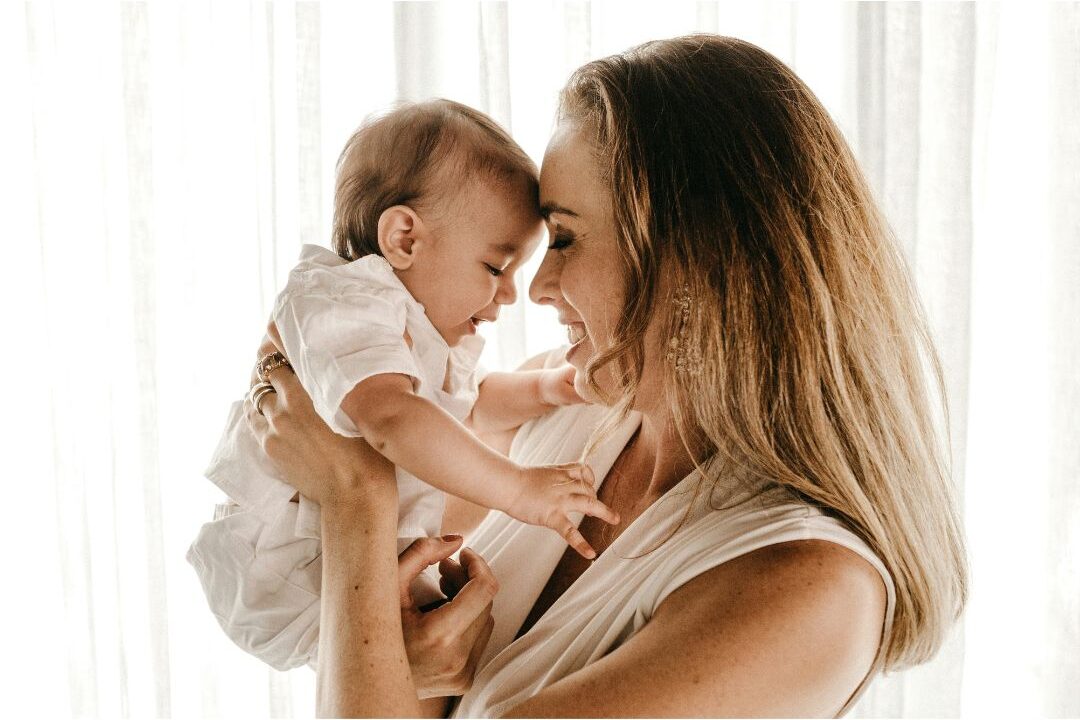 mother holding child warmly smiling near bright sunny window embracing unfiltered motherhood