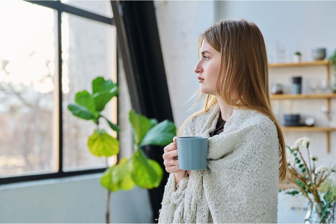 woman looking out sunlit window peacefully holding a warm mug demonstrating how to love staying home again