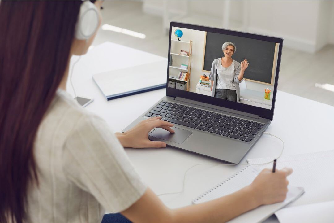 woman taking notes while watching an online course video on her laptop screen