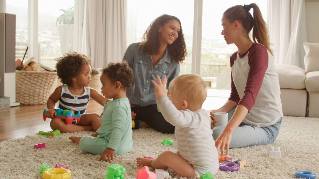mother chatting with friend over coffee while kids play nearby showing adult connection