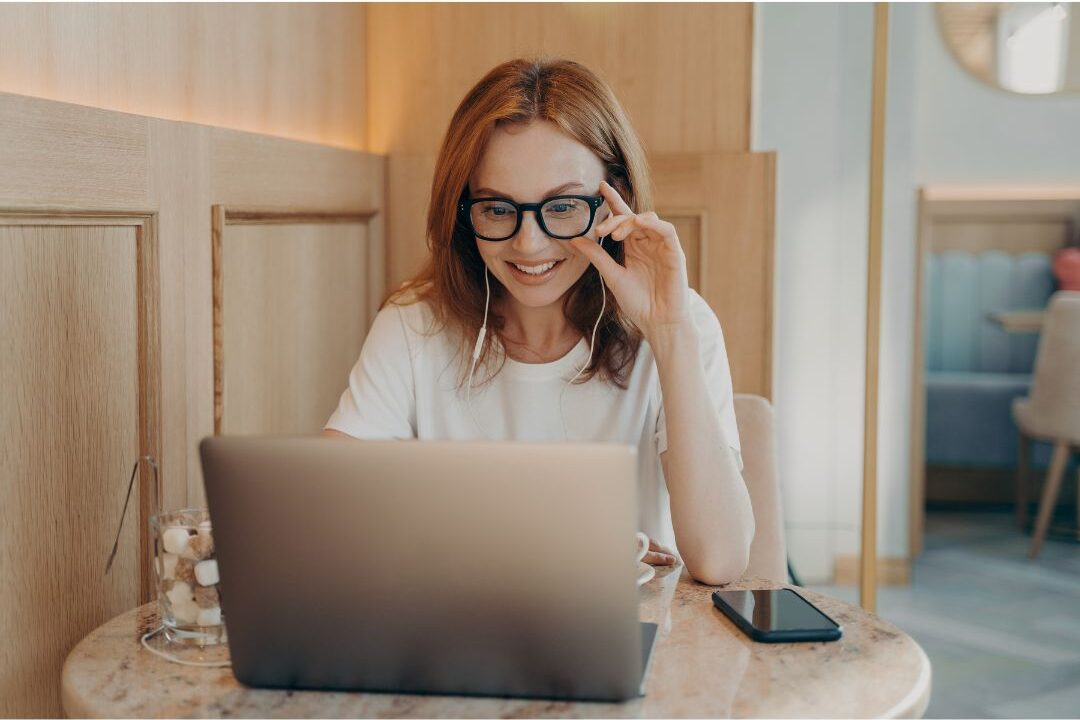 woman looking at her laptop screen smiling in a home office reflecting on things I wish I knew before starting my first side hustle