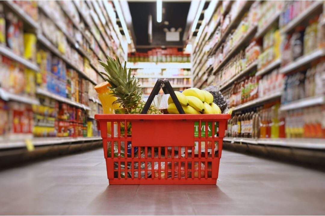 grocery shopping cart filled with packaged food items in a supermarket aisle