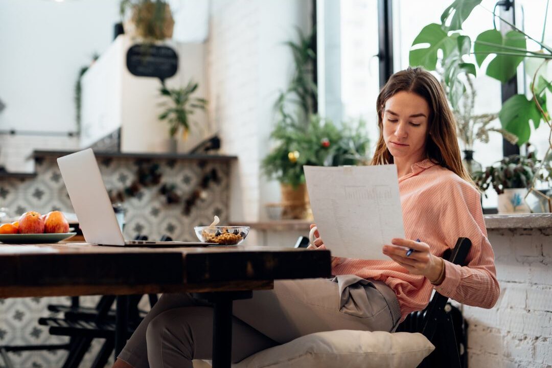 thoughtful woman sitting at a kitchen table reviewing bank statements to find the hidden expenses quietly destroying your budget