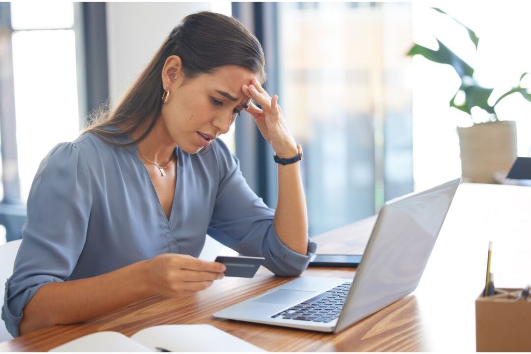 woman holding a credit card looking concerned at her computer screen