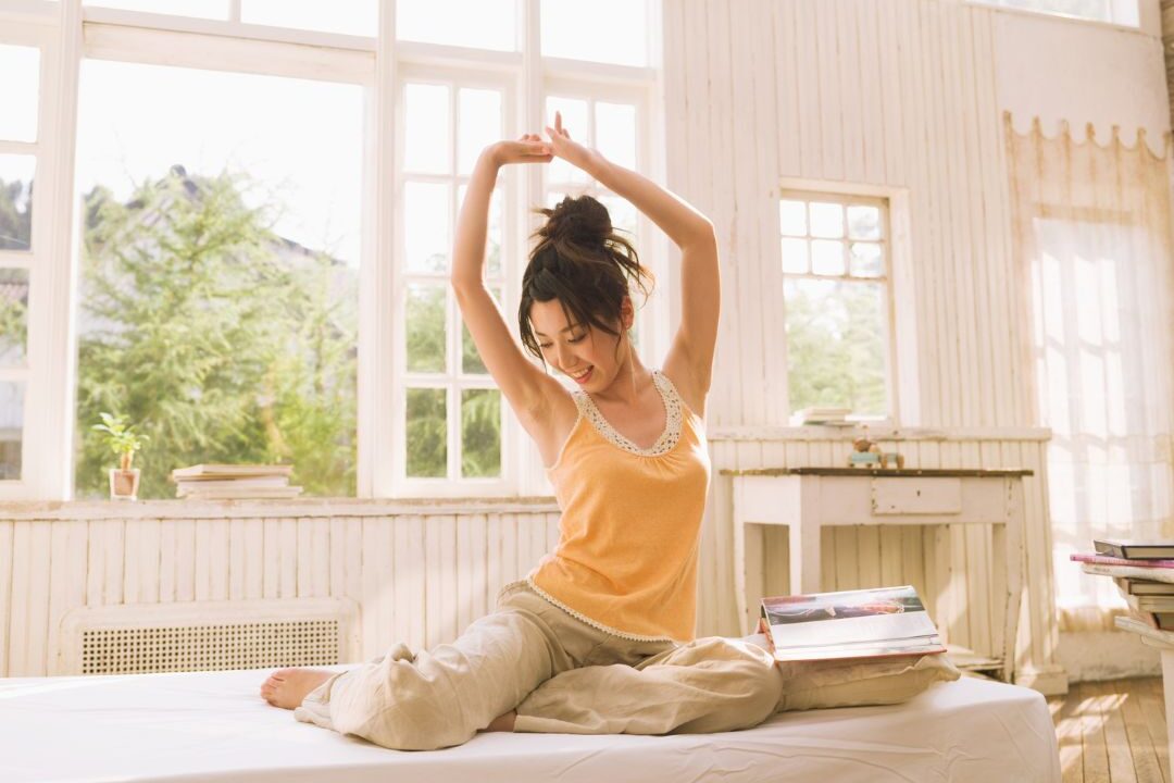 woman stretching gently near sunlit bedroom window on rug honoring physical recovery