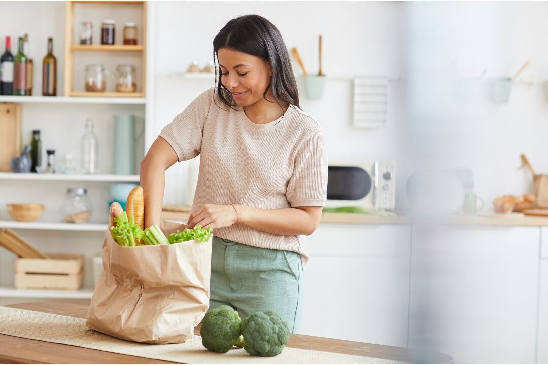 smiling woman unpacking healthy grocery bags on a clean kitchen island showing how we cut our grocery bill in half