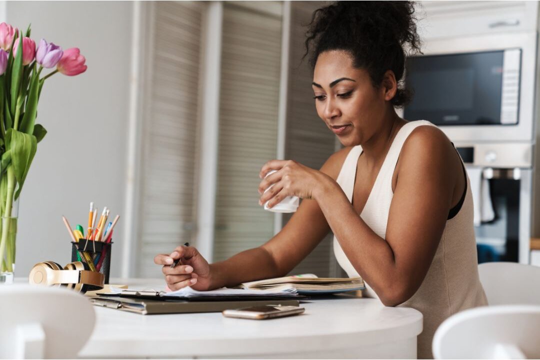 woman sitting at kitchen island writing in planner with coffee managing the hidden challenges nobody warns moms about