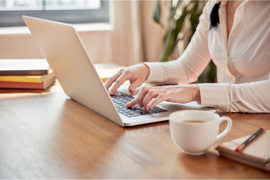 woman calmly typing on a laptop with a notebook beside her illustrating the launch plan steps