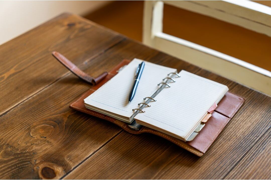 warm sunlit desk with open leather journal and elegant pen showing daily planning