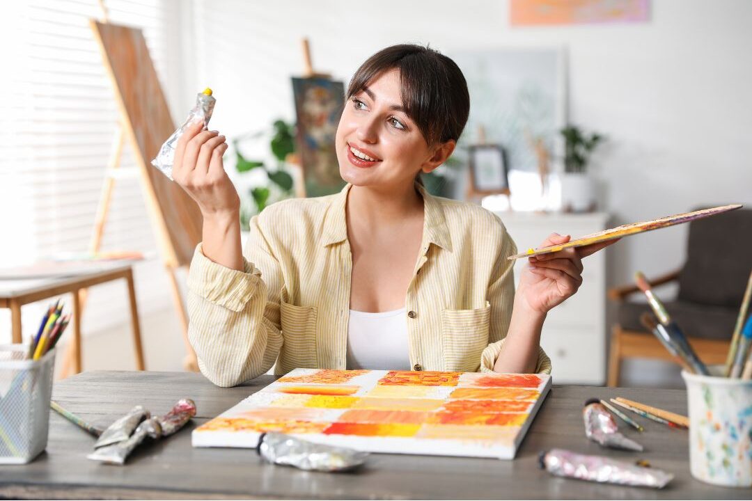 woman painting on a small canvas at a wooden table enjoying creative time