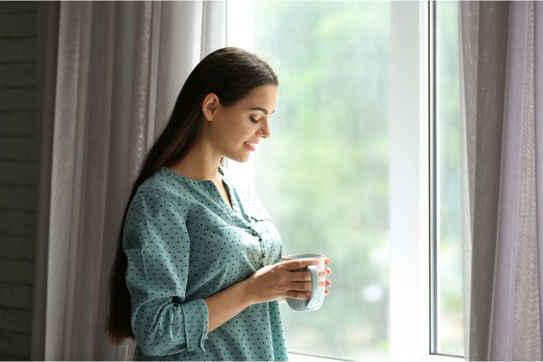 peaceful woman drinking tea near window in soft sunlight practicing luxury habits anyone can afford