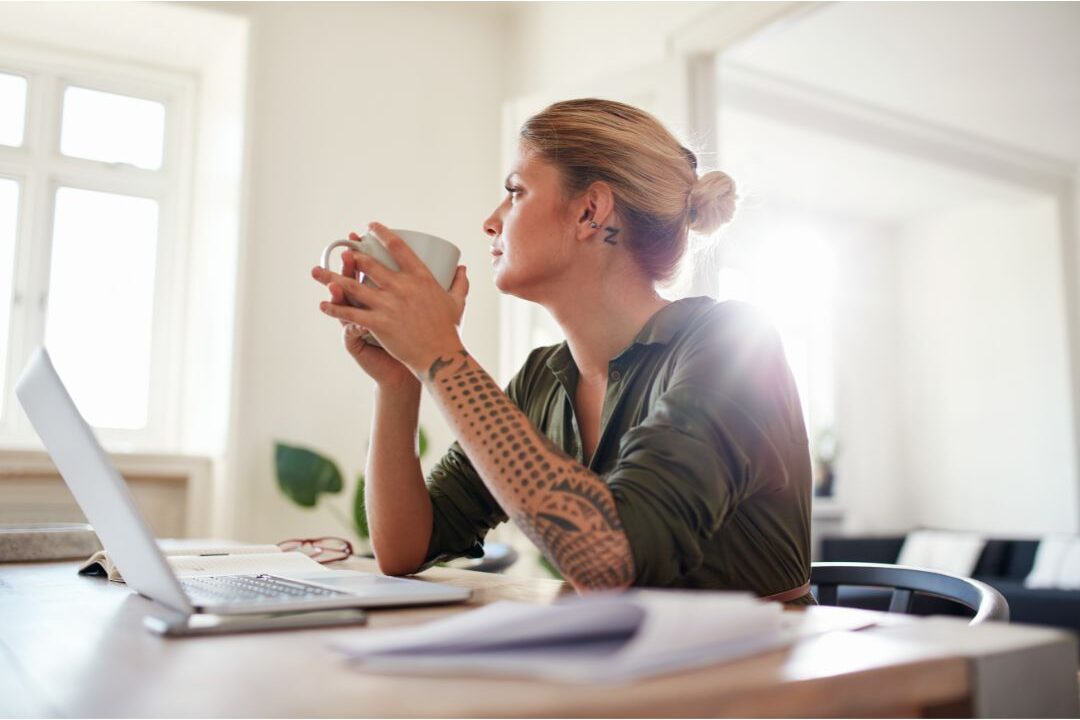 woman sitting thoughtfully at home desk with laptop and coffee navigating hidden challenges nobody warns moms about