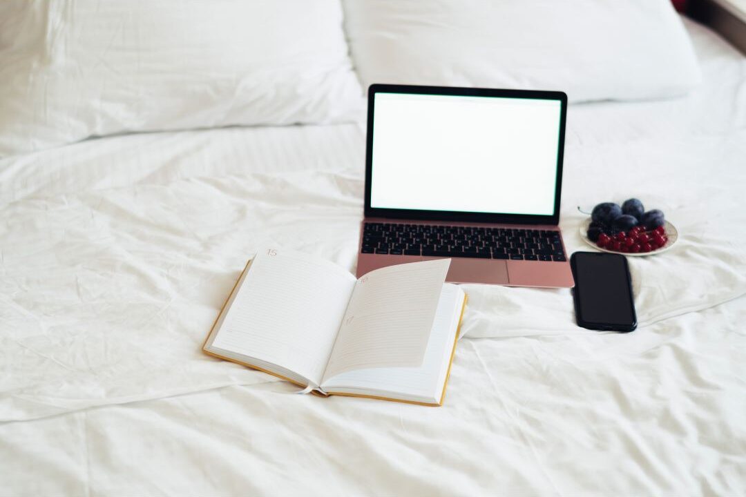 smartphone lying beside open book on soft linen bed highlighting how you are wasting 3 hours every day