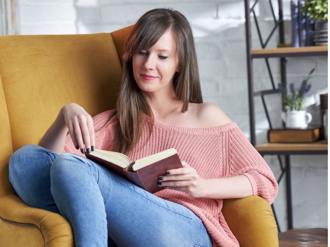 woman sitting in cozy sunlit armchair reading a book illustrating luxury habits anyone can afford
