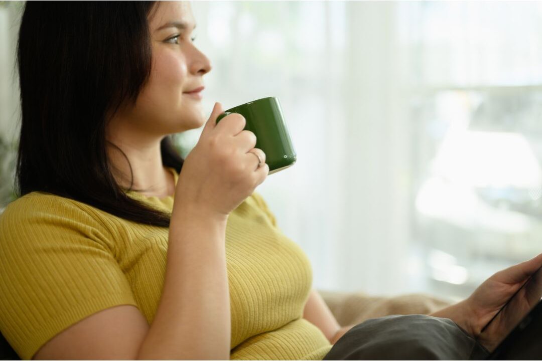 woman looking thoughtfully out window while holding warm mug showing emotional reflection
