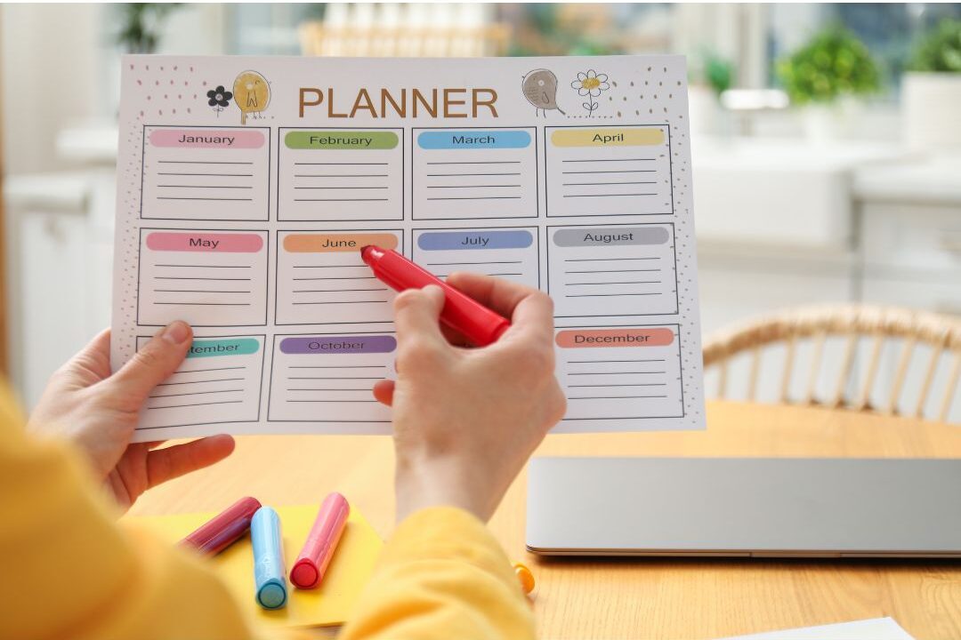 woman writing a meal planner schedule at a wooden kitchen table demonstrating how we cut our grocery bill in half