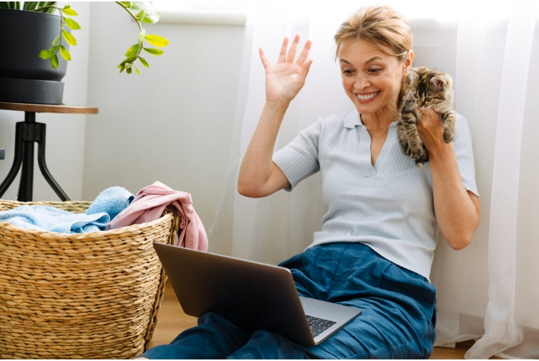 woman trying to type on laptop while holding laundry basket experiencing multi-tasking stress