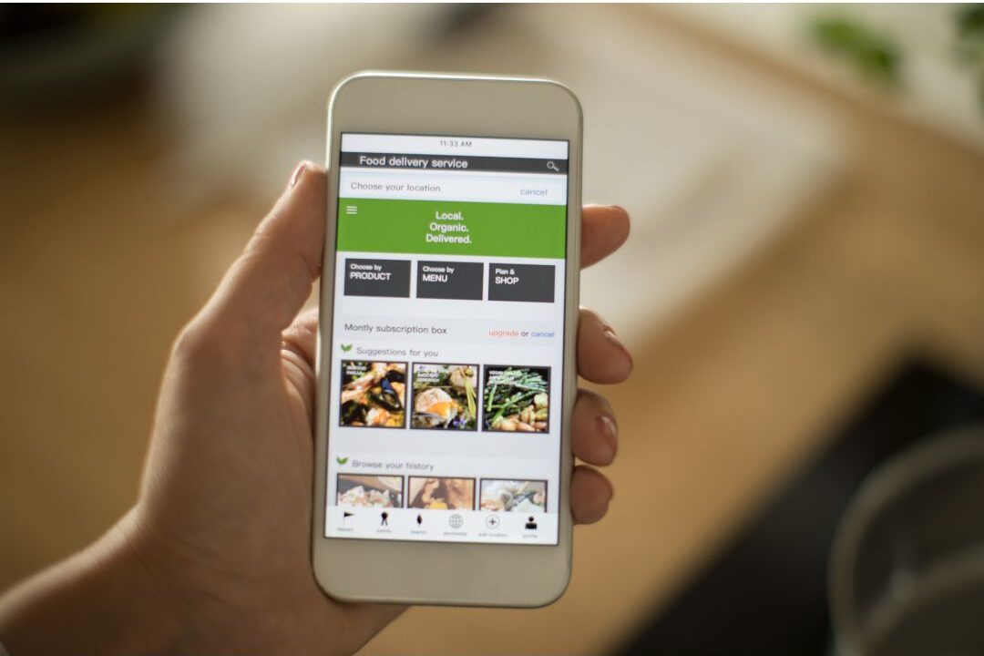 woman selecting grocery items on a mobile phone app at her kitchen table