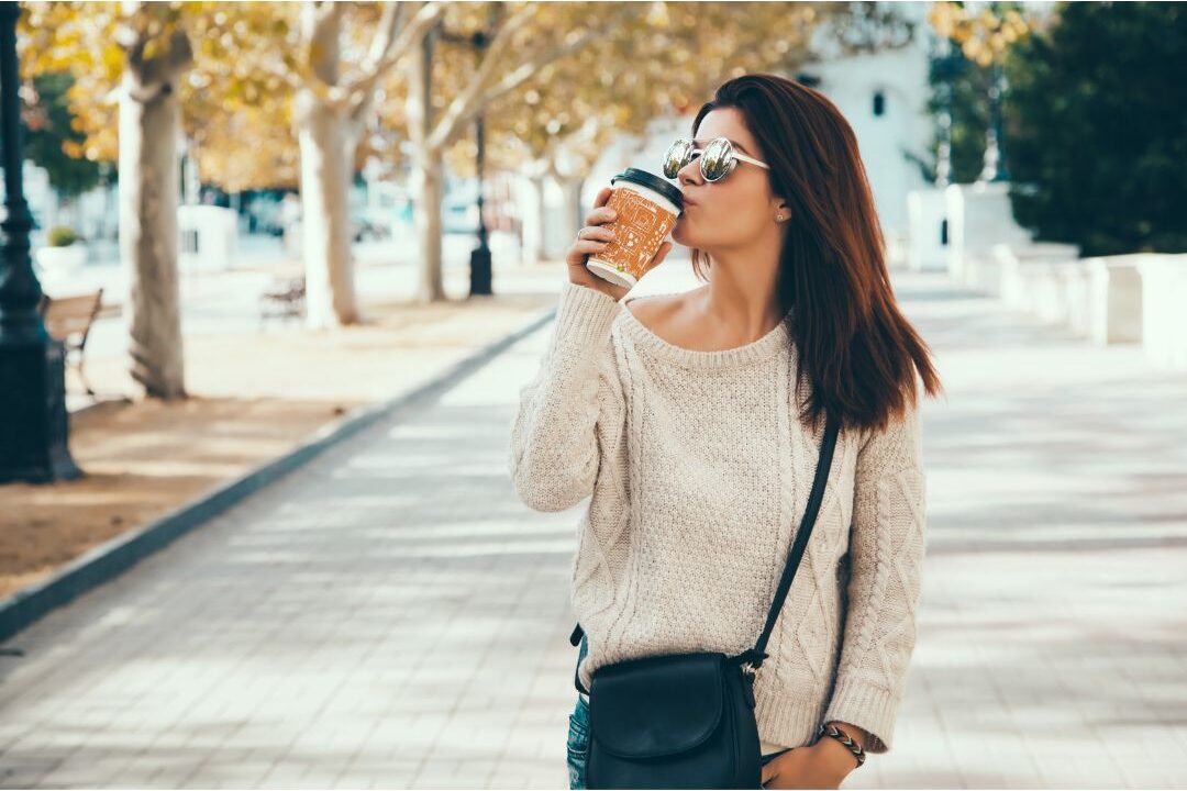 woman walking in quiet green park holding morning coffee avoiding things stay at home moms need to hear