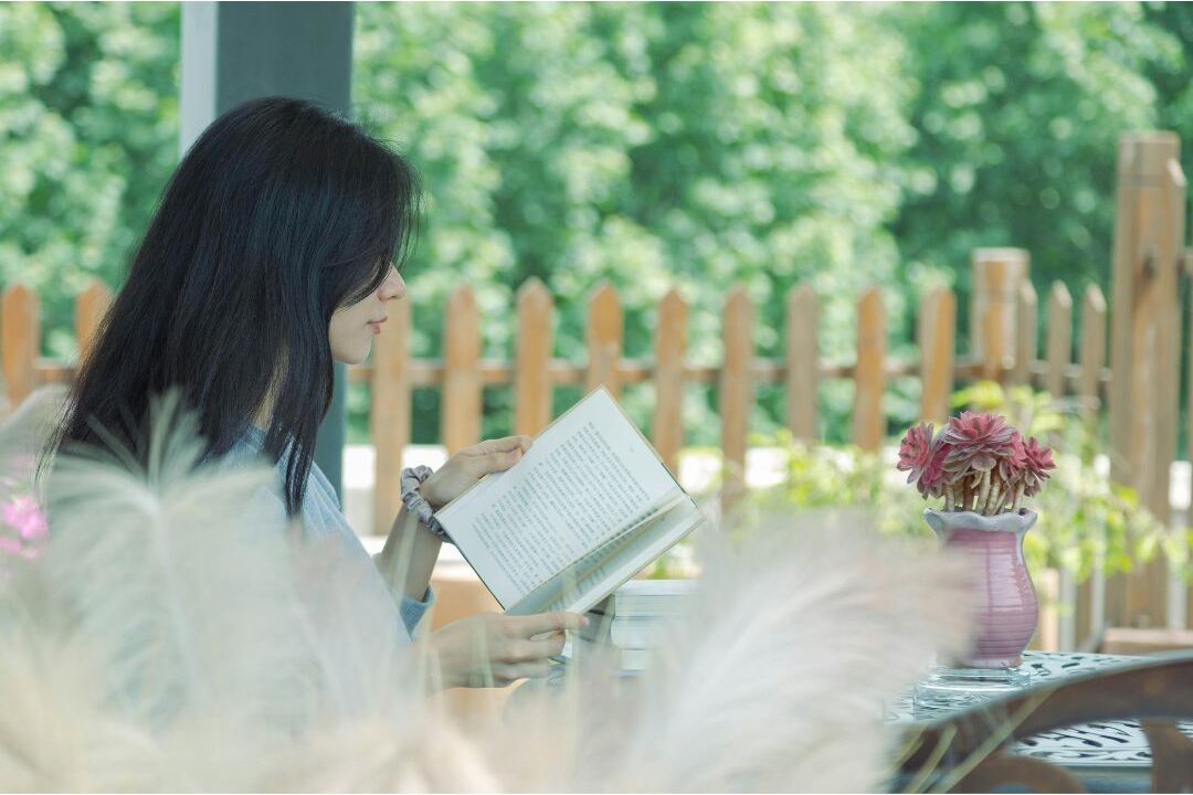 woman sitting outdoors on sunny porch reading a book peacefully overcoming the hard truth about being home all day