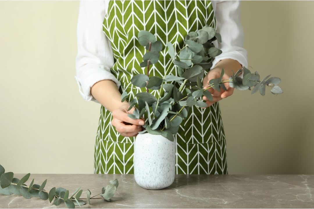 woman placing fresh green branches into tall ceramic vase on table practicing things that instantly make your home look expensive