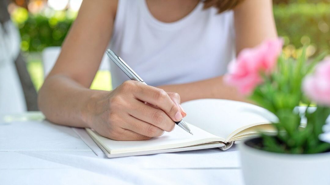 woman writing thoughtfully in notebook at warm sunlit table planning daily changes
