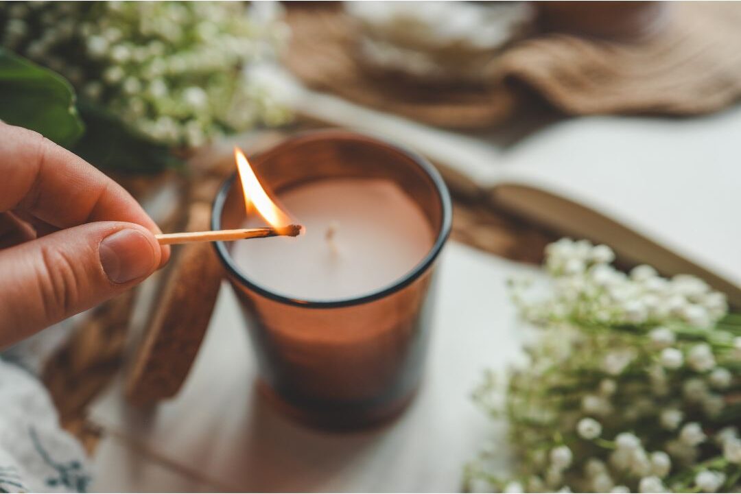 woman lighting a scented candle on a clean bedside nightstand executing luxury habits anyone can afford