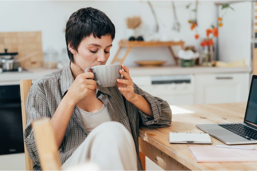woman sitting peacefully at kitchen table with notebook and warm drink resolving wasting 3 hours every day