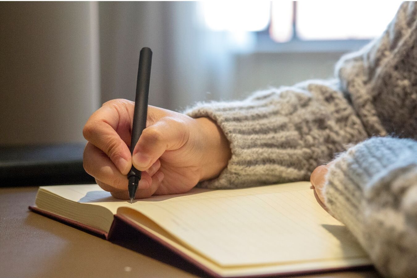 woman writing thoughtfully in notebook at warm sunlit table creating morning plan